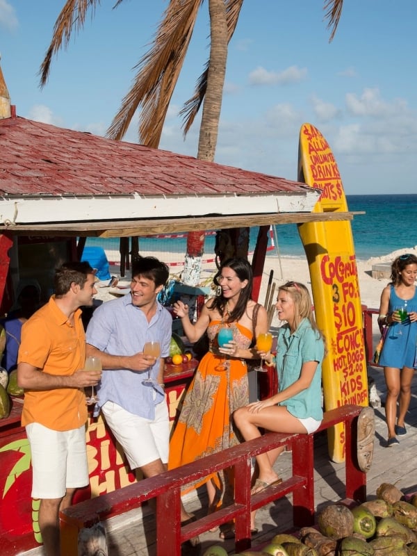A group of friends laughs and enjoys tropical beverages at a bar on the beach in The Bahamas. 