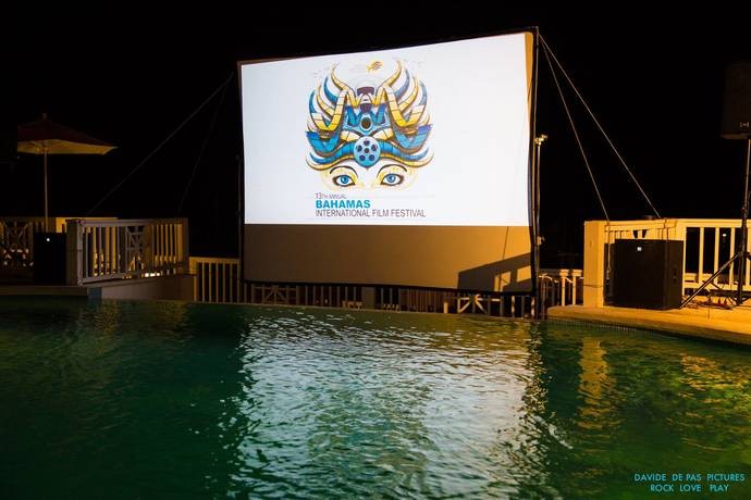 A movies screen with the Bahamas International Film Festival logo is set up next to a pool.