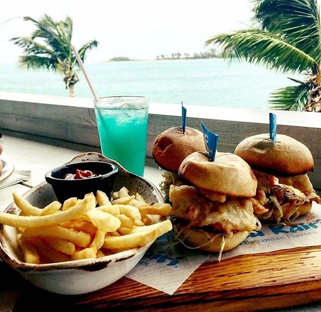 French fries, burgers and a blue icy beverage sit atop a beach-side table.