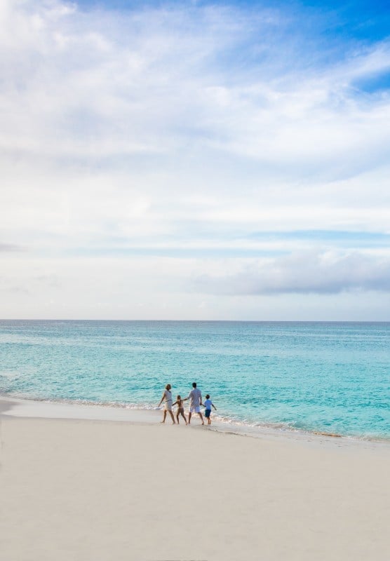 A family of four walks hand-in-hand along a Bahamas beach.