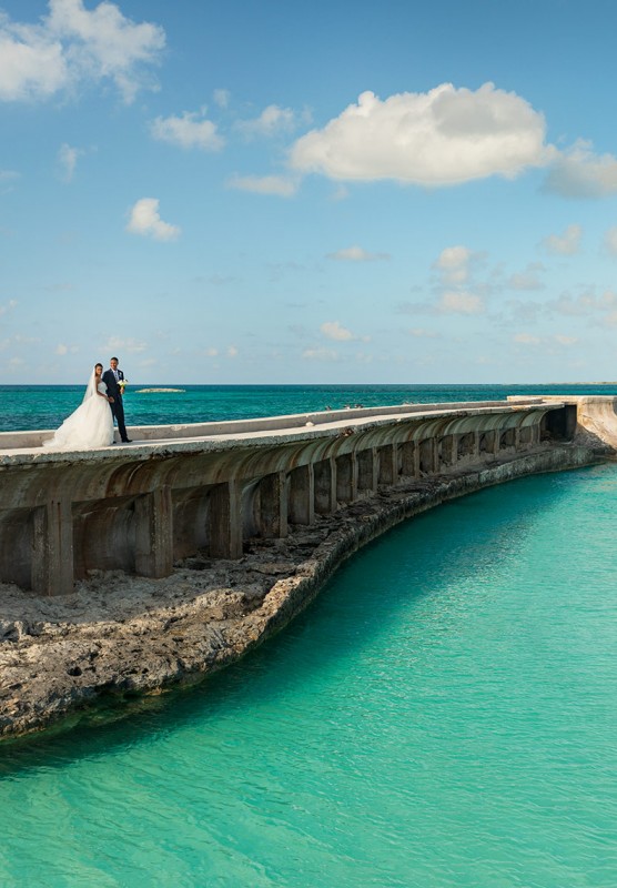 A bride and groom stand on a boardwalk that runs alongside a small river