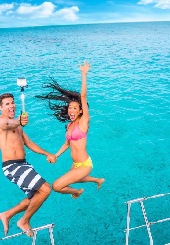 A couple jumps into the water while holding a selfie stick.