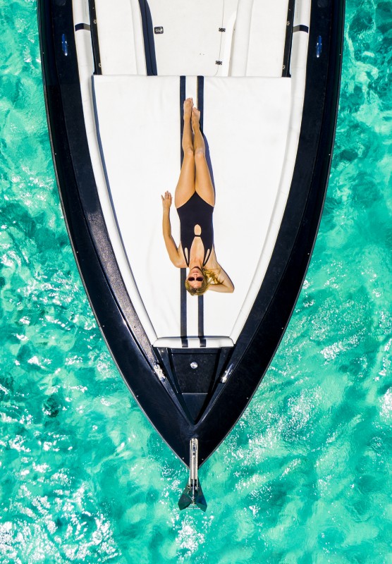 A woman relaxes on a boat deck floating on bright turquoise waters. 