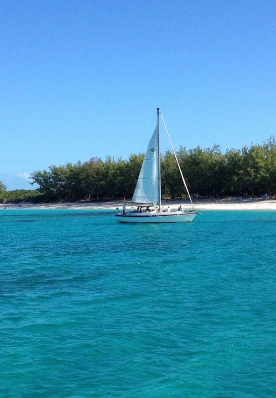 A sailboat sailing towards a white sand beach in crystal clear waters.