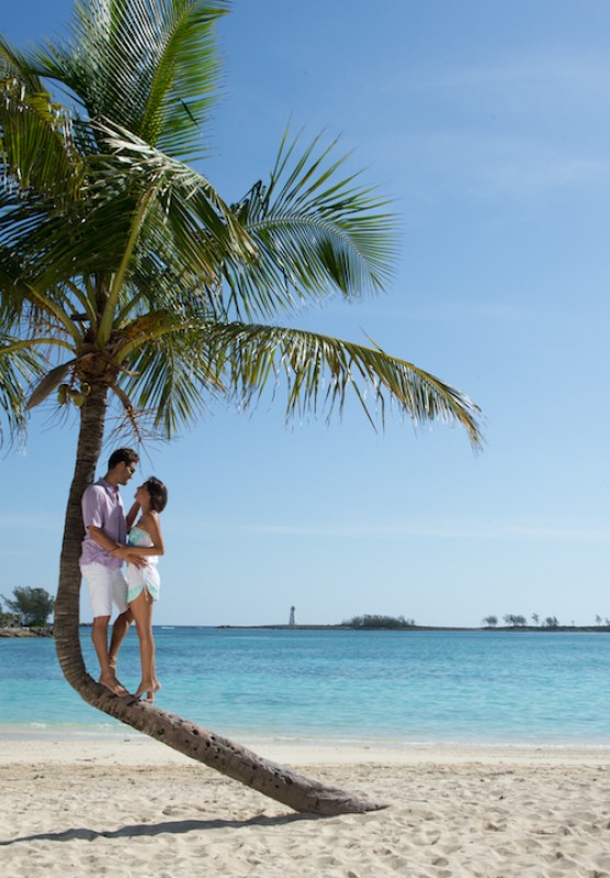 A couple relaxes under the shade of a palm tree on a Bahamas beach