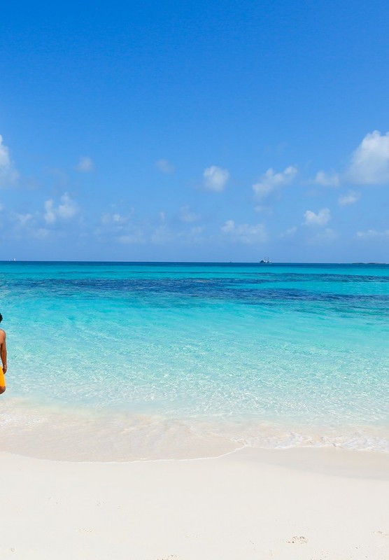 A man and woman walk hand-in-hand down a white sand beach.