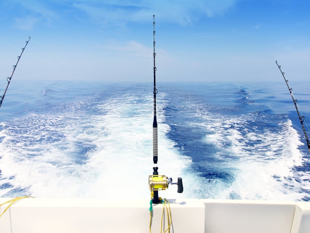 Four fishing rods attached to the back of a moving fishing boat sailing through blue waters.