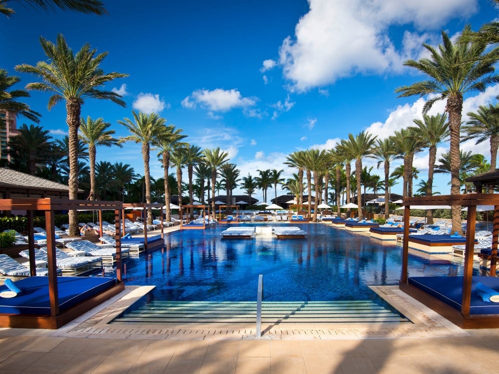 A couple relax on a large lounge chair by the pool on a sunny day.