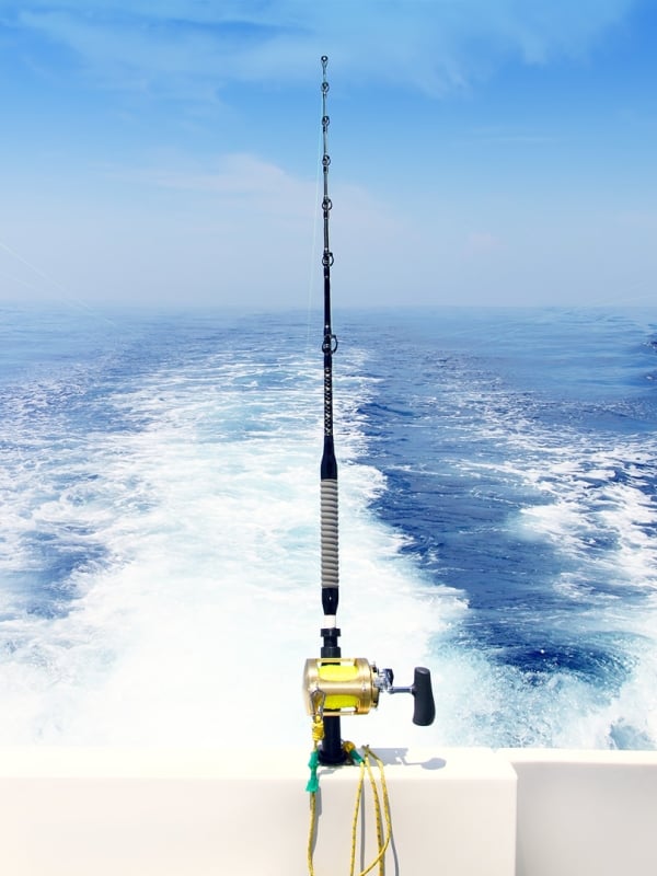 Four fishing rods attached to the back of a moving fishing boat sailing through blue waters.