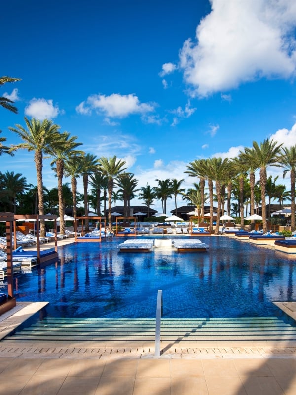 A couple relax on a large lounge chair by the pool on a sunny day.